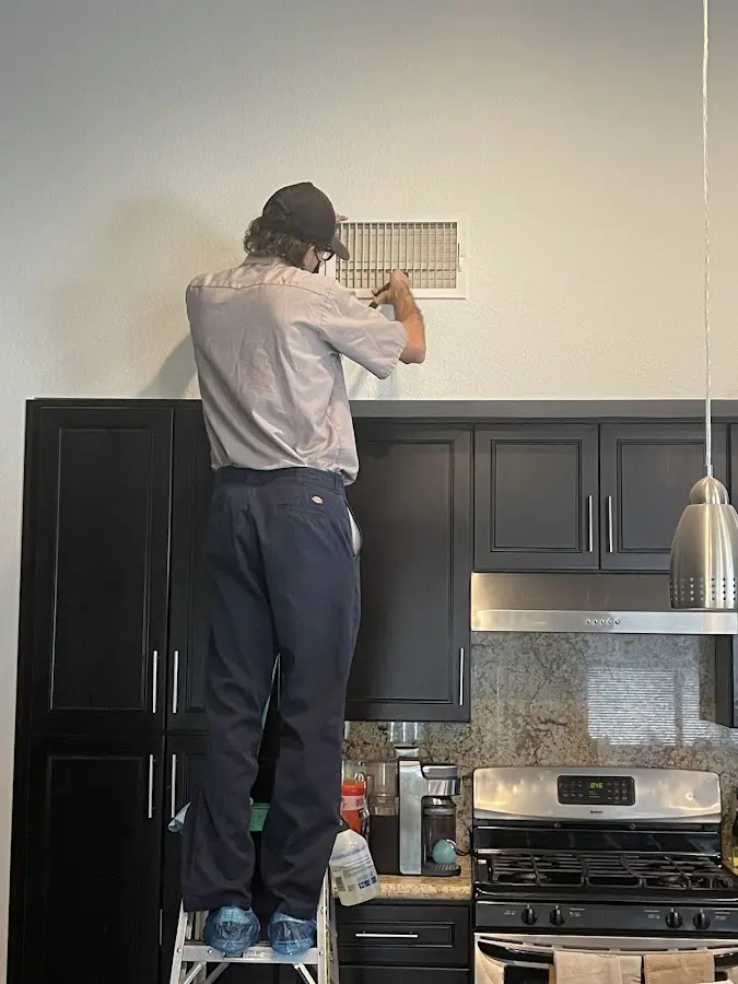 Technician inspecting an air vent during HVAC service in Orchard Mesa